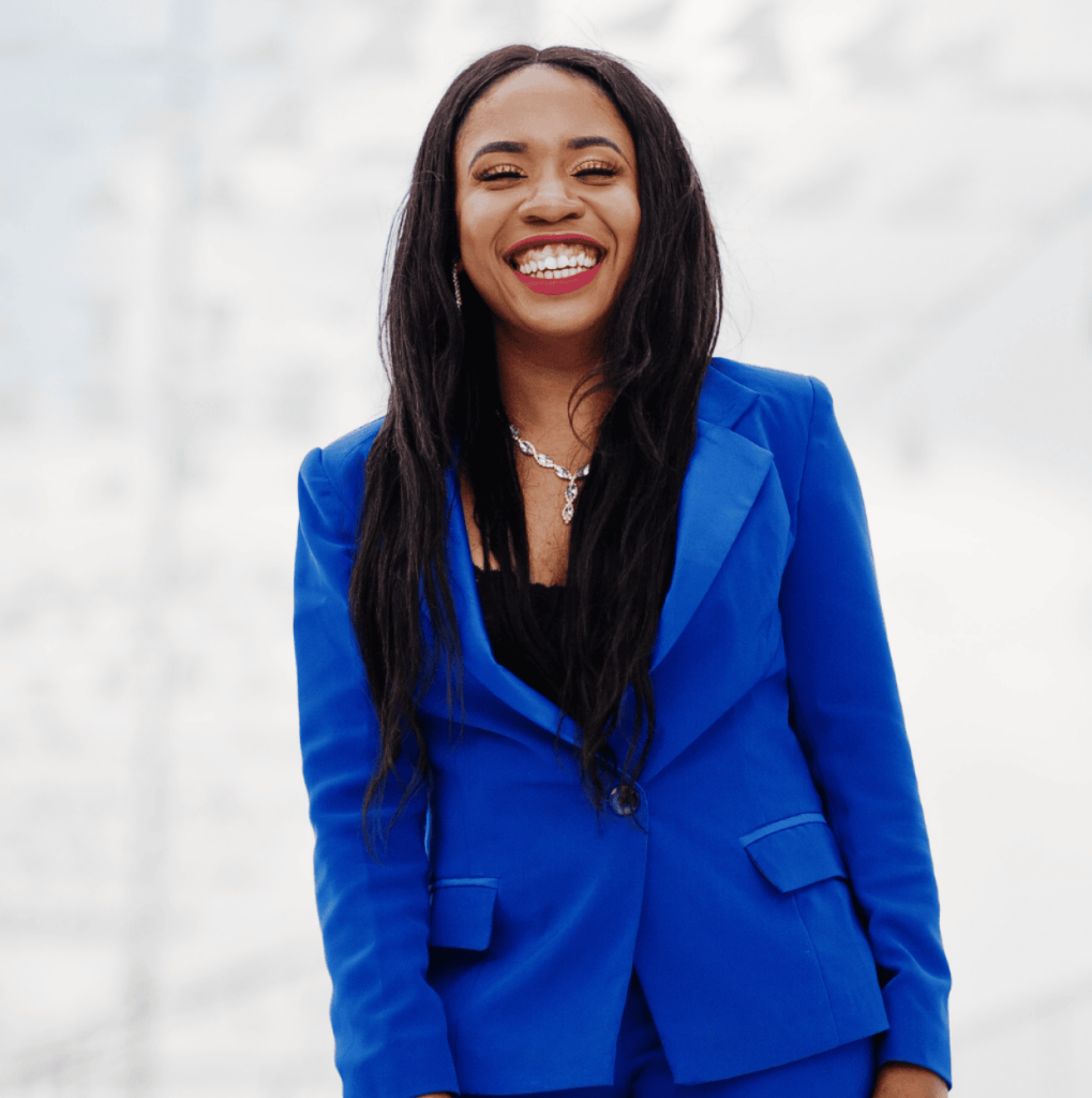 A smiling professional standing outdoors in a bright blue suit, conveying confidence, wellbeing, and international readiness.
