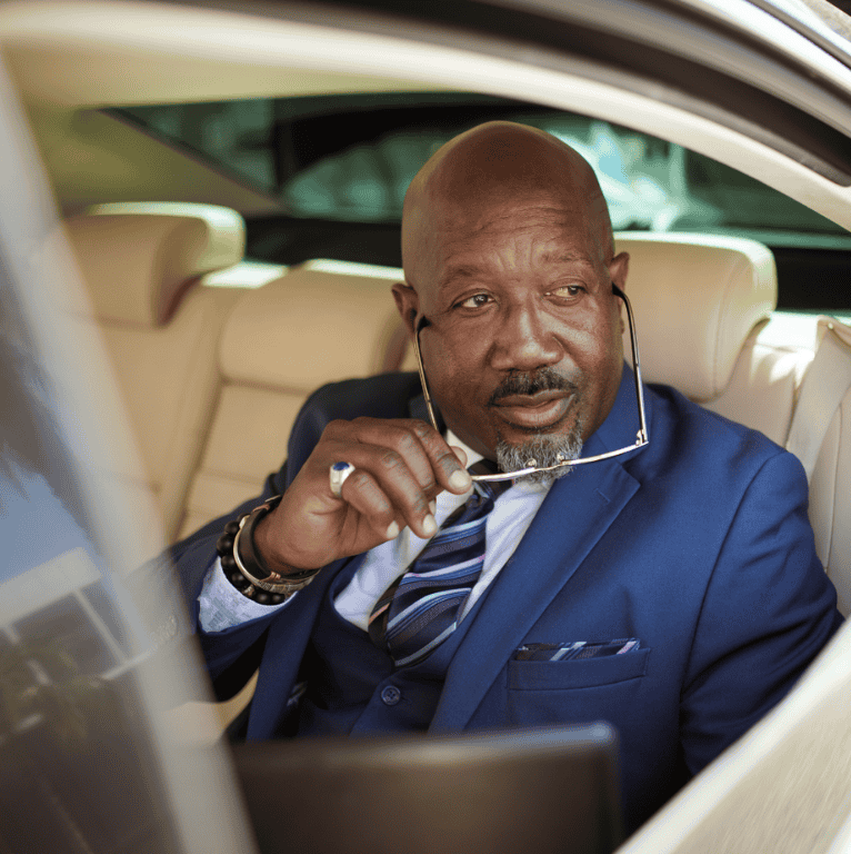 A professional seated in the back of a car, dressed in a suit and holding eyeglasses, conveying confidence and international mobility