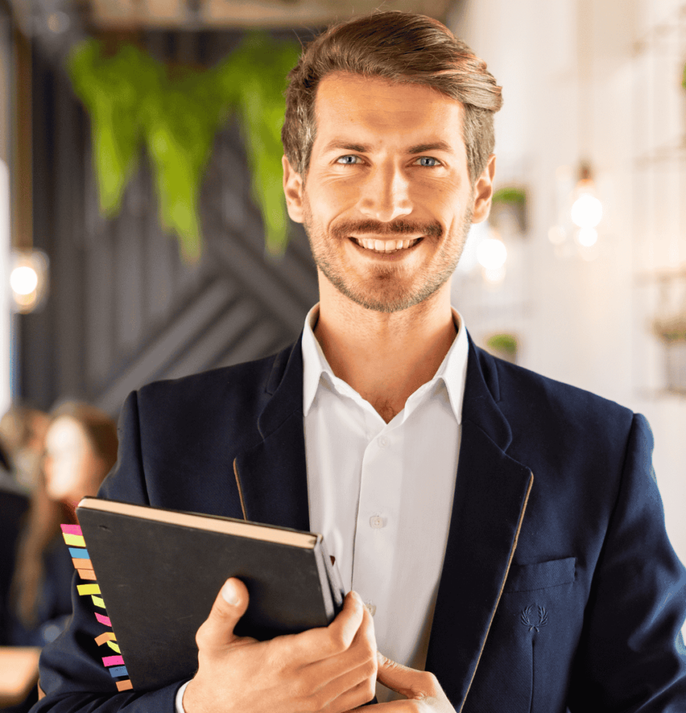 A professional holding a notebook in a modern, well‑lit interior, dressed in a dark blazer and white shirt, conveying confidence and refined professionalism