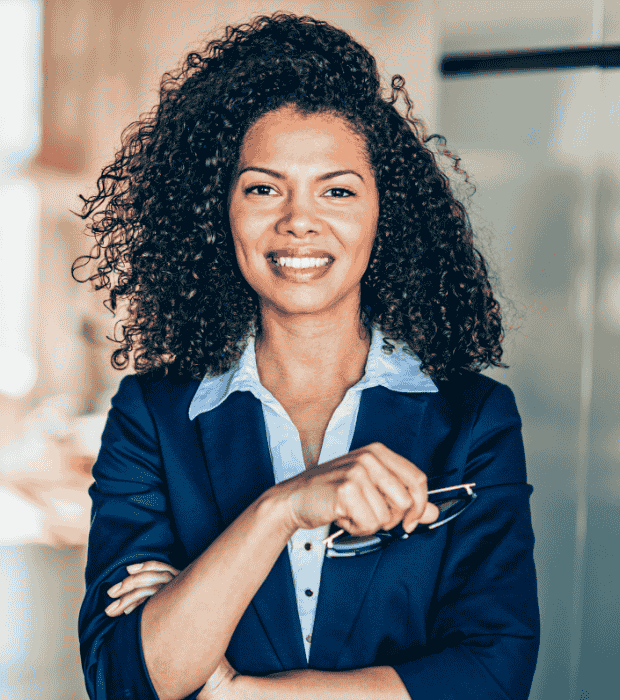 A confident professional smiling while holding eyeglasses in a modern, softly lit interior space.